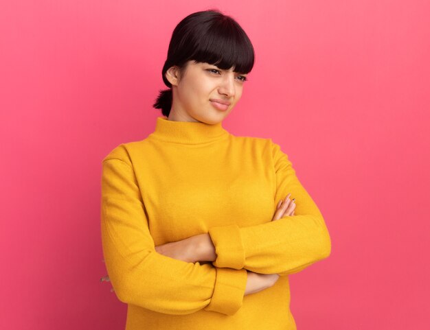 Insatisfait jeune fille caucasienne brune se tient avec les bras croisés à côté sur rose