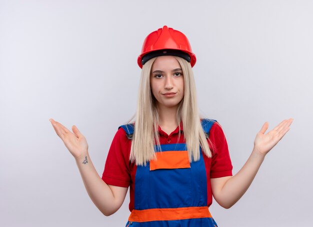 Insatisfait jeune fille de constructeur ingénieur blonde en uniforme montrant les mains vides sur un mur blanc isolé