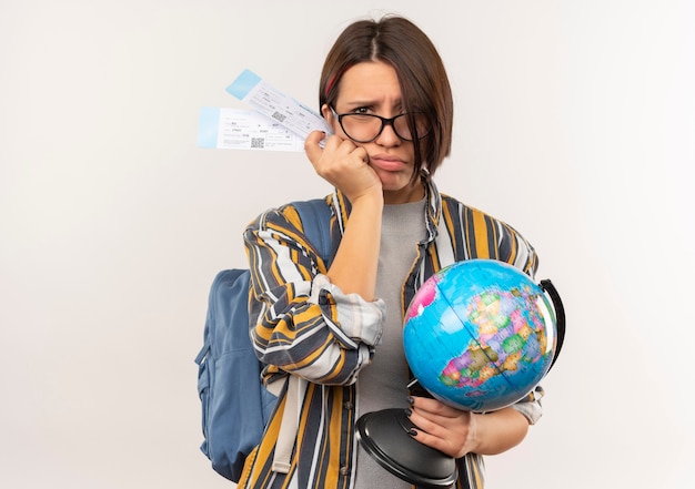 Insatisfait jeune fille étudiante portant des lunettes et sac à dos tenant des billets d'avion et globe isolé sur fond blanc avec espace de copie