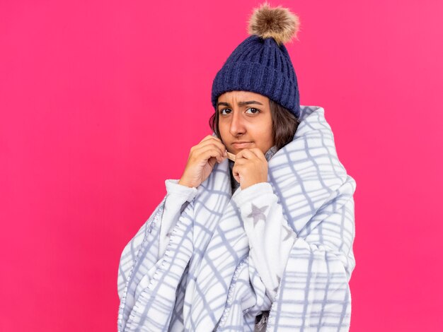 Insatisfait jeune fille malade portant chapeau d'hiver avec écharpe enveloppée de plaid mettant du plâtre sur le nez isolé sur fond rose