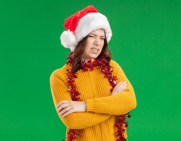 Insatisfait jeune fille slave avec bonnet de Noel et avec guirlande autour du cou se dresse avec les bras croisés