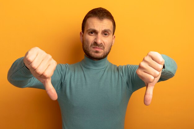 Insatisfait jeune homme caucasien montrant les pouces vers le bas isolé sur un mur orange