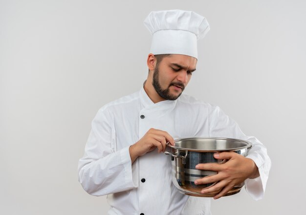 Insatisfait jeune homme cuisinier en uniforme de chef tenant et regardant pot isolé sur espace blanc