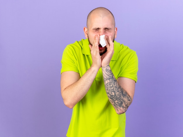 Insatisfait jeune homme malade de race blanche essuie le nez avec du tissu isolé sur un mur violet avec copie espace