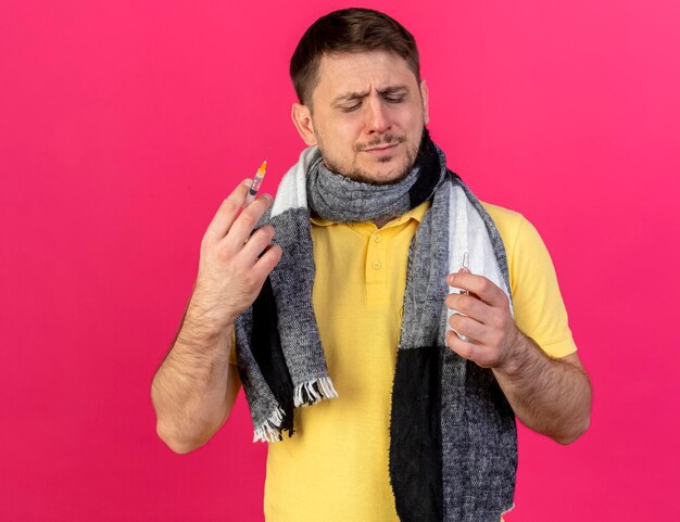 Insatisfait jeune homme slave malade blonde portant un foulard détient une seringue et une ampoule sur rose