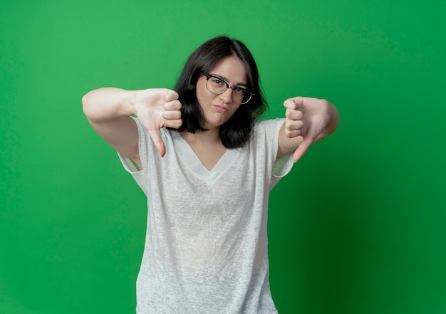 Photo gratuite insatisfait jeune jolie fille caucasienne portant des lunettes montrant les pouces vers le bas isolé sur fond vert avec copie espace