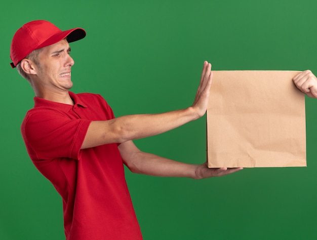 Photo gratuite insatisfait jeune livreur blonde donne un paquet de papier à quelqu'un sur le vert
