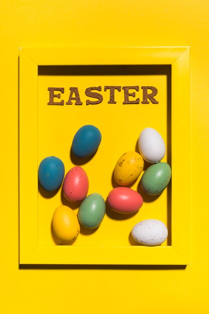 Inscription de Pâques dans le cadre avec des oeufs colorés sur une table jaune