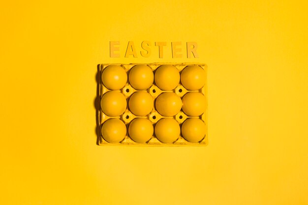 Photo gratuite inscription de pâques avec des oeufs en rack sur une table jaune