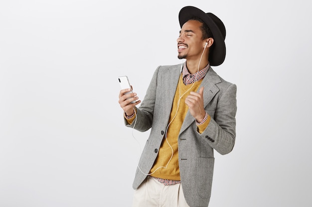 Insouciant danse homme afro-américain, écouter de la musique dans les écouteurs, souriant et tenant le smartphone