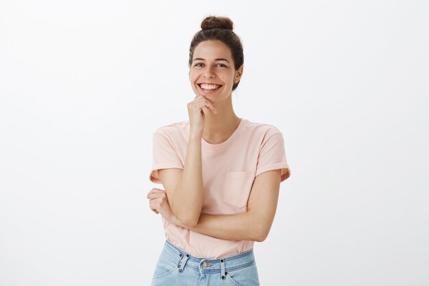 Insouciante jeune femme élégante posant contre le mur blanc