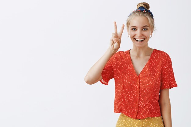 Insouciante jeune fille blonde posant contre le mur blanc