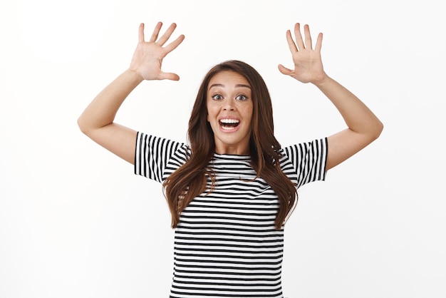 Insouciante Jeune Fille Heureuse Sautant Du Bas Et Levant Les Mains Vers Le Haut Montre Dix Doigts Souriant Optimiste S'amusant à L'air Ludique Et Ravi Debout Fond Blanc En T-shirt Rayé