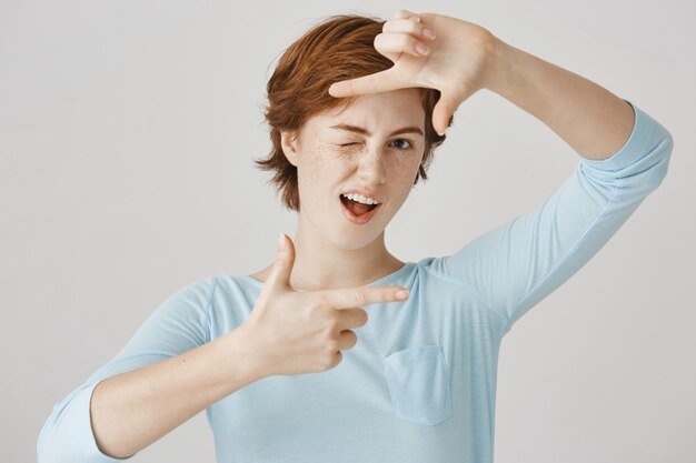 Insouciante jolie fille rousse posant contre le mur blanc