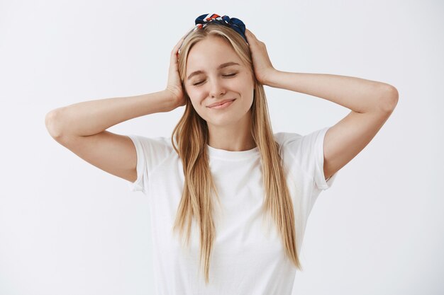 Insouciante jolie jeune fille blonde posant contre le mur blanc