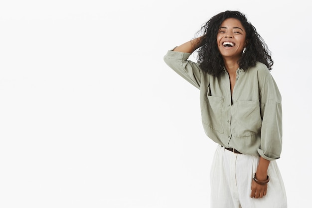 Insouciante ravie et heureuse femme afro-américaine créative en chemise à la mode et pantalon tenant la main sur les cheveux