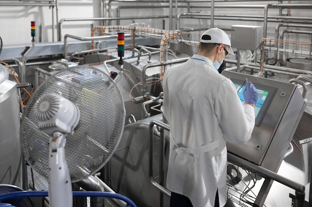 Inspecteur dans un masque et un gommage se tient avec un dossiertablette dans ses mains à l'usine laitière