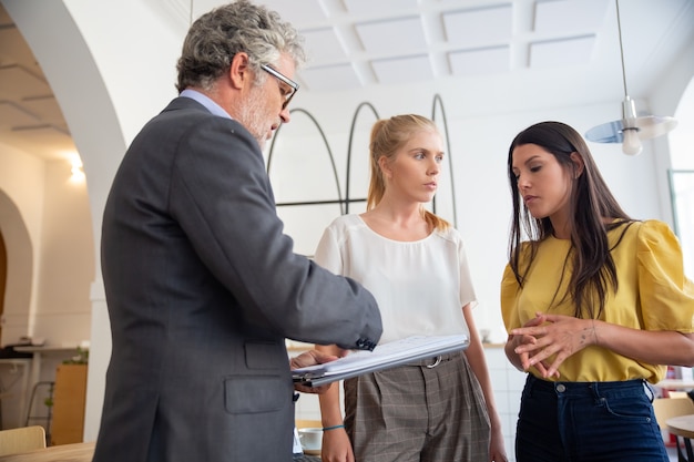 Inspecteur de prêt mature avec bloc-notes visitant de jeunes entrepreneurs sur place