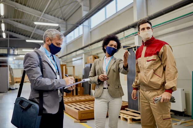 Des inspecteurs du contrôle de la qualité parlent à un travailleur masculin lors d'une visite à l'usine de menuiserie pendant la pandémie de coronavirus