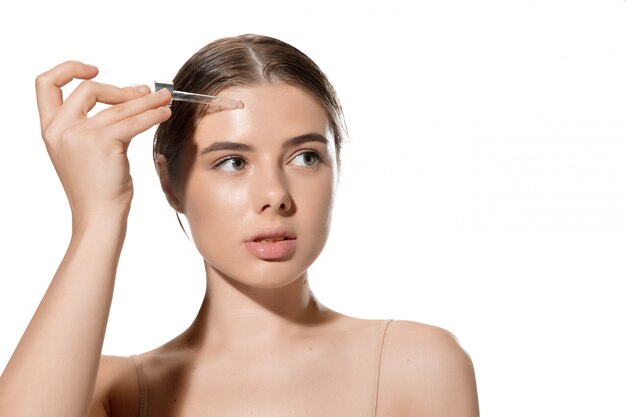 Inspiré. Gros plan de la belle jeune femme avec des feuilles vertes sur son visage sur blanc. Cosmétique et maquillage, soin naturel et éco, soin de la peau