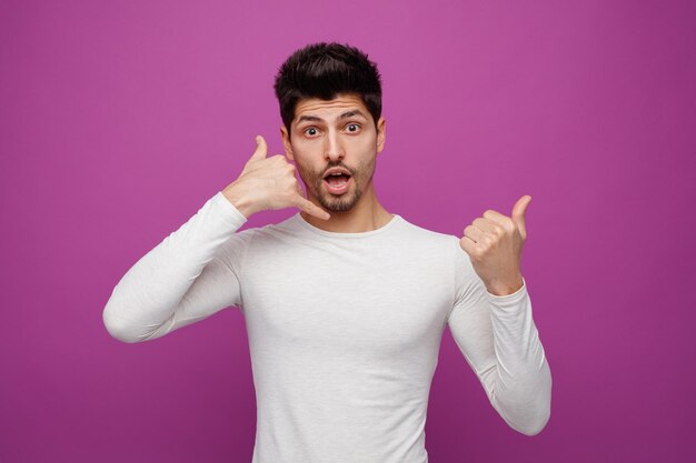 Inspiré d'un jeune bel homme regardant la caméra faisant un téléphone pointant vers un geste latéral sur fond violet