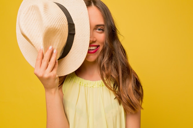 Inspiré jolie femme aux longs cheveux ondulés couvrant son visage avec un chapeau