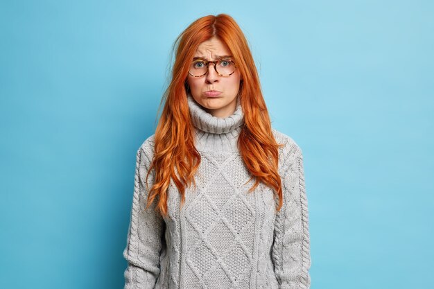 Insulté mécontent de la femme européenne au gingembre a offensé l'expression des bourses à lèvres et veut pleurer habillé en pull gris porte des lunettes.