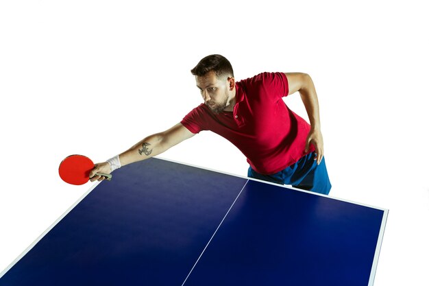 Intense. Jeune homme joue au tennis de table sur mur blanc. Le modèle joue au ping-pong. Concept d'activité de loisirs, sport, émotions humaines dans le jeu, mode de vie sain, mouvement, action, mouvement.