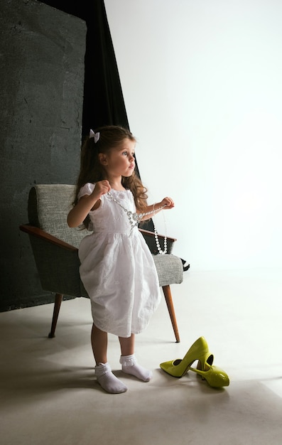 Interaction des enfants avec le monde des adultes. Jolie fille portant les chaussures surdimensionnées de maman et s'habillant pour être plus âgée comme elle l'est. Petit modèle féminin essayant des vêtements à la maison. Enfance, style, concept de rêve.