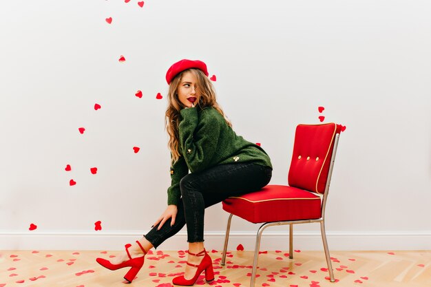 Intéressé femme galbée en pull vert posant en studio décoré de coeurs