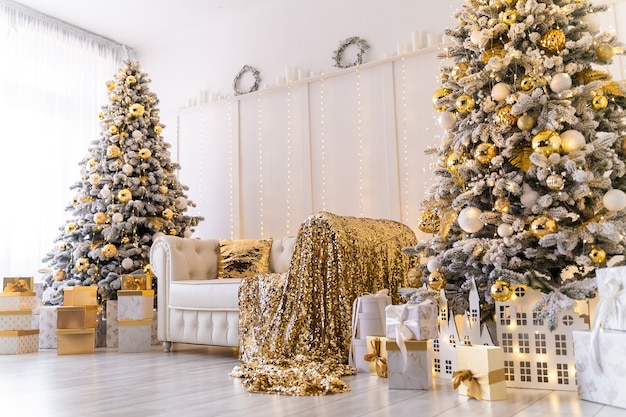 Intérieur de noël blanc moderne avec deux arbres de noël décorés de cadeaux dorés en textile doré