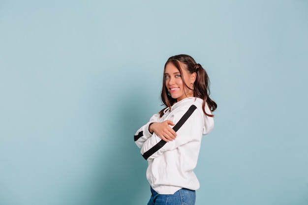 À l'intérieur, portrait, de, sourire, jolie jeune femme, à, cheveux noirs, porter, blanc, pullover, poser, sur, mur isolé