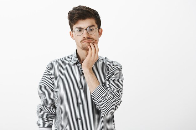 Interrogé un homme barbu attrayant douteux avec une moustache dans des lunettes rondes, tenant la main sur le menton et regardant vers le bas tout en pensant ou en espaçant pendant la conversation, en étant loin de la discussion