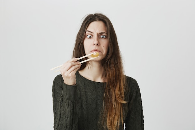 Intrigué fille drôle regardant la mandarine qu'elle tient avec des baguettes