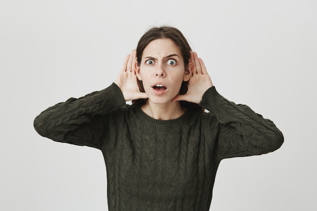 Intrigué mignonne jeune femme se tenir la main près des oreilles, écoute clandestine, comme des rumeurs