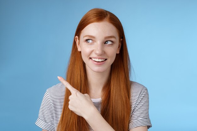 Intriguée belle rousse joyeuse fille curieuse regardant regarder le coin supérieur gauche intéressé souriant largement visiter un endroit amusant et cool explorer un nouveau pays étonné, fond bleu.