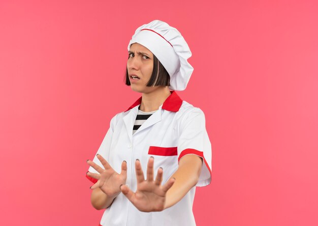 Inutile de jeune femme cuisinier en uniforme de chef gesticulant pas à la caméra isolée sur fond rose avec copie espace