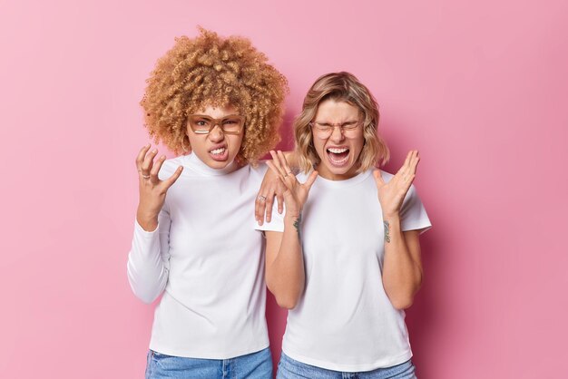 Irrité deux jeunes femmes amis geste avec colère se sentir ennuyé s'exclamer bruyamment dérangé par un son trop fort porter des vêtements blancs isolés sur fond rose Concept de personnes et d'émotions négatives