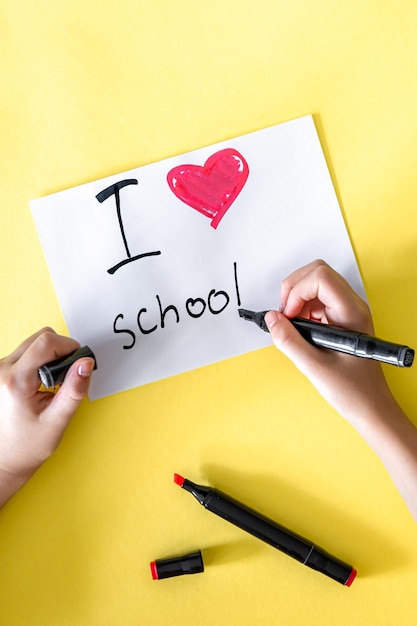 J'adore l'école la main de l'enfant écrit dans un papier sur un fond jaune