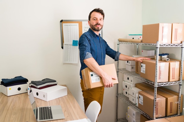 J'ai une entreprise en pleine croissance. Portrait d'un bel entrepreneur souriant et établissant un contact visuel tout en préparant des colis prêts à être expédiés aux clients