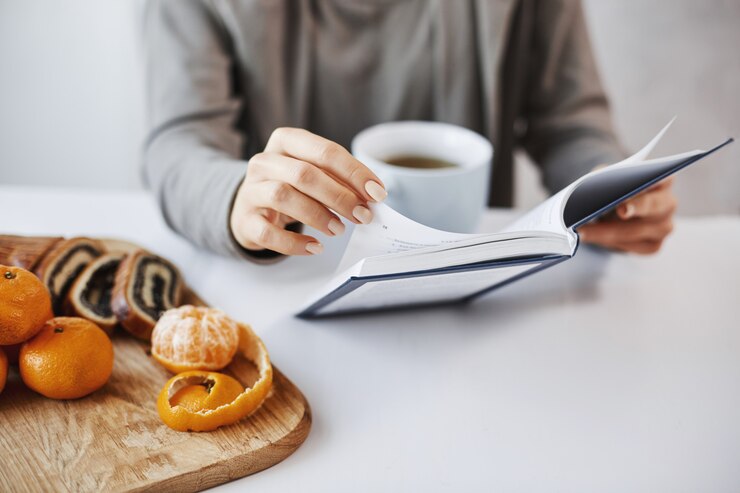 Photo gratuit j'ai hâte de lire tout le livre. la fille est amoureuse de l'histoire écrite sur des pages de roman, déjeune, boit du thé avec des mandarines et du gâteau roulé. employé de bureau ayant une pause après avoir rencontré des clients