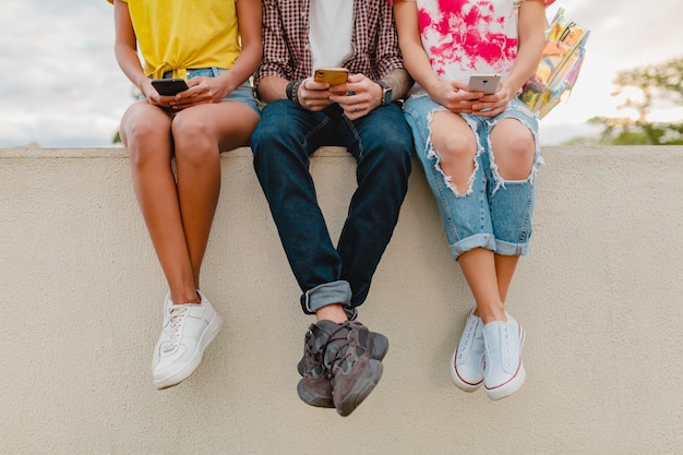 Jambes en baskets de jeune entreprise d'amis assis park à l'aide de smartphones