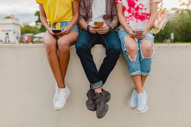 Photo gratuite jambes en baskets de jeune entreprise d'amis assis park à l'aide de smartphones