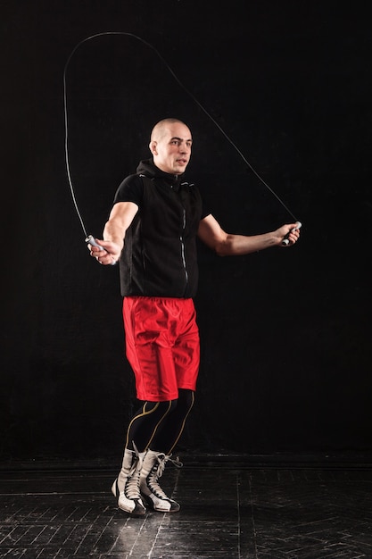 Les jambes de l'homme musclé avec entraînement à la corde à sauter kickboxing sur fond noir