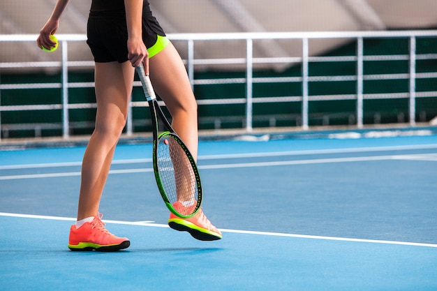 Jambes de jeune fille dans un court de tennis fermé avec balle et raquette