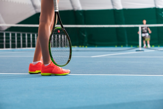 Photo gratuite jambes de jeune fille dans un court de tennis fermé avec balle et raquette