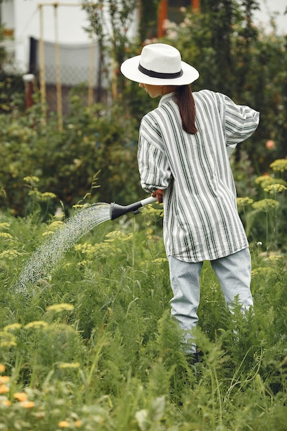 Jardinage en été. Femme arrosage des fleurs avec un arrosoir. Fille portant un chapeau.