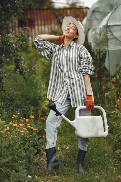 Jardinage en été. Femme arrosage des fleurs avec un arrosoir. Fille portant un chapeau.