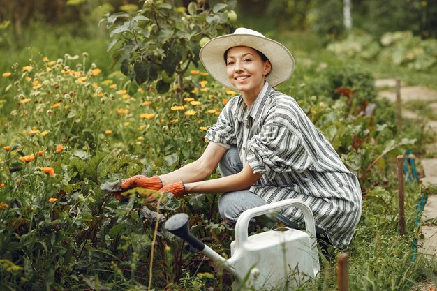 Jardinage en été. Femme arrosage des fleurs avec un arrosoir. Fille portant un chapeau.