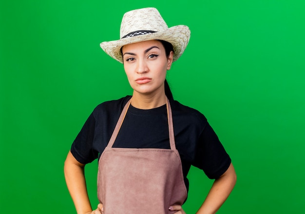 Jardinier de belle jeune femme en tablier et chapeau avec une expression sceptique sérieuse